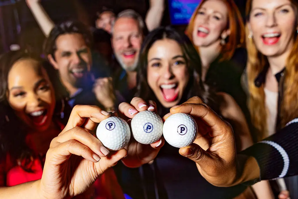 3 Puttshack golf balls being held up in front of a group of guests